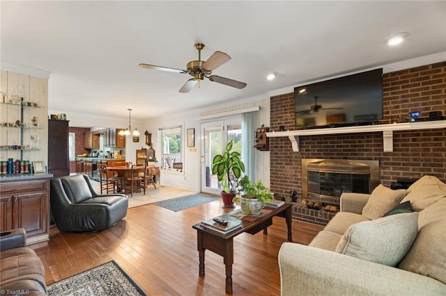 living room featuring ornamental molding, a ceiling fan, hardwood / wood-style floors, brick wall, and a fireplace