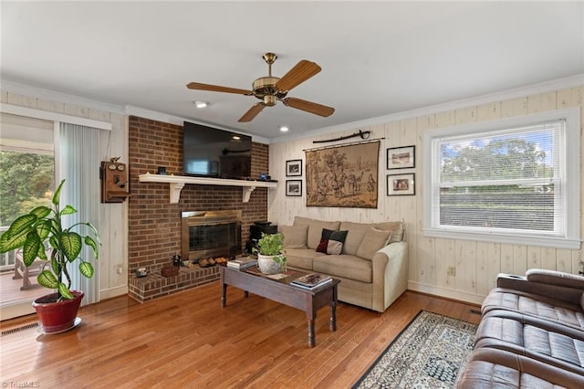 living room featuring visible vents, a brick fireplace, ceiling fan, ornamental molding, and wood finished floors