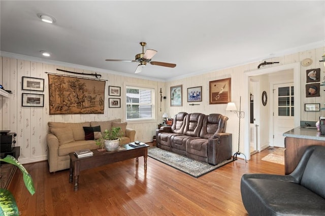 living room featuring baseboards, wood finished floors, a ceiling fan, and ornamental molding