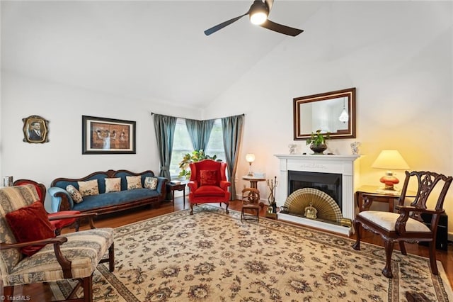 living area featuring wood finished floors, high vaulted ceiling, a fireplace with raised hearth, and ceiling fan