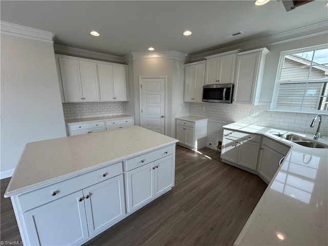 kitchen with sink, white cabinetry, ornamental molding, dark hardwood / wood-style flooring, and a kitchen island