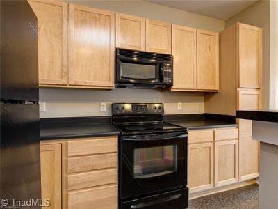 411 W Washington St Unit 309, Greensboro, NC 27401 - kitchen featuring black appliances, light brown cabinets, and dark countertops