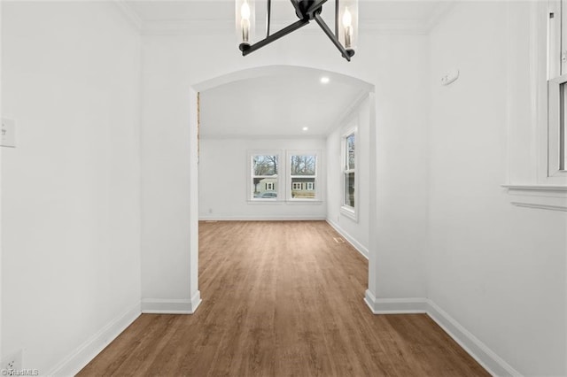 hall featuring baseboards, arched walkways, and crown molding