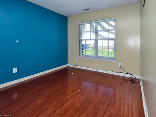 spare room featuring wood finished floors, visible vents, and baseboards