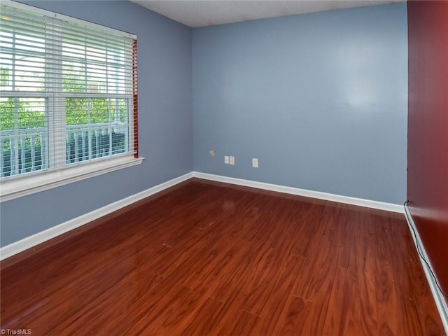 unfurnished room with baseboards and dark wood-style floors