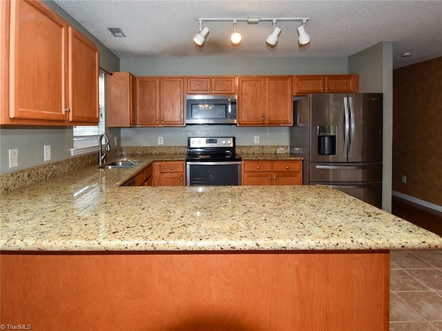 kitchen with a sink, light stone countertops, a peninsula, appliances with stainless steel finishes, and tile patterned flooring