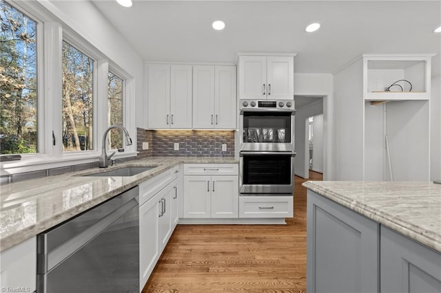 kitchen featuring light wood-type flooring, a sink, light stone counters, backsplash, and stainless steel appliances