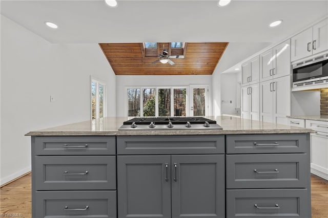 kitchen with vaulted ceiling with skylight, white cabinets, appliances with stainless steel finishes, and gray cabinetry