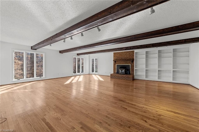 unfurnished living room with beam ceiling, track lighting, a textured ceiling, wood finished floors, and a brick fireplace