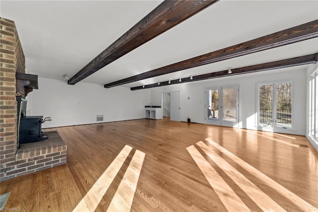 unfurnished living room featuring wood finished floors, visible vents, a wood stove, french doors, and beamed ceiling