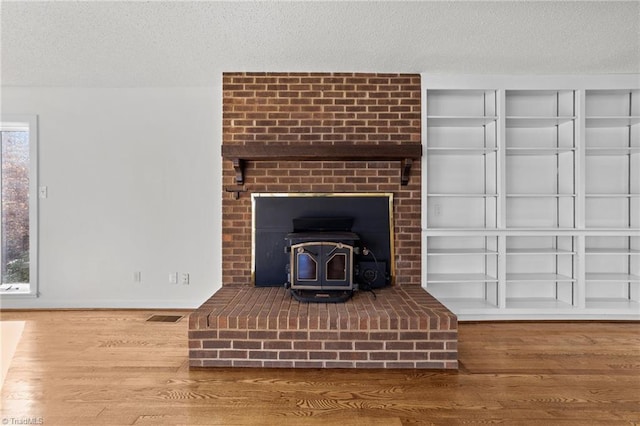 interior details featuring wood finished floors, baseboards, visible vents, a wood stove, and a textured ceiling