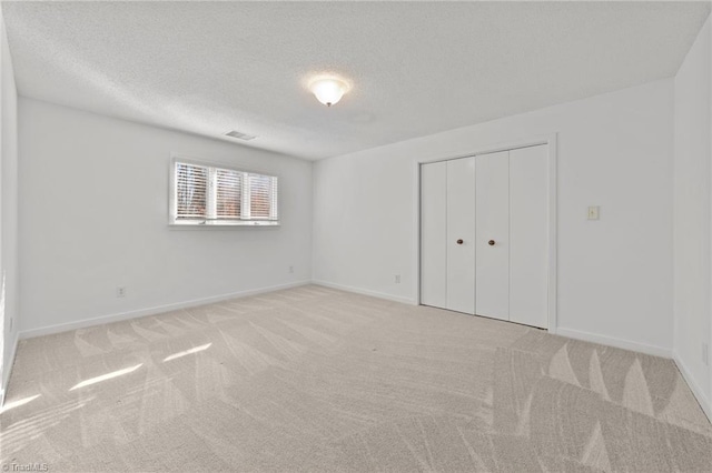 unfurnished bedroom featuring visible vents, light carpet, a textured ceiling, and baseboards