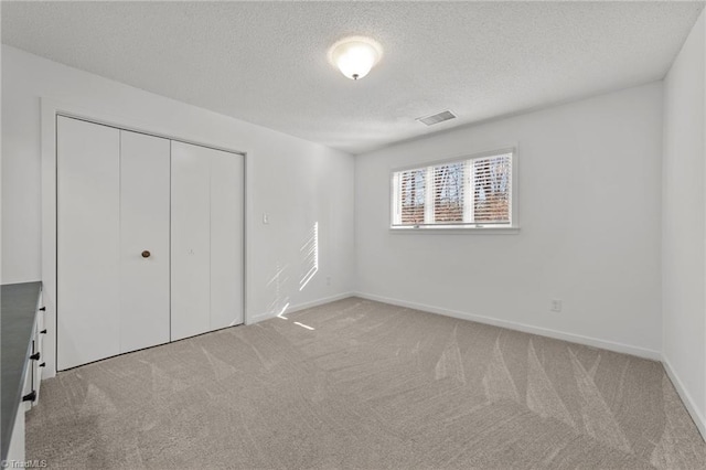 unfurnished bedroom with baseboards, visible vents, a closet, a textured ceiling, and light carpet