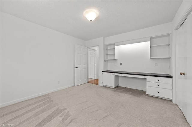 unfurnished office featuring a textured ceiling, light carpet, baseboards, and built in study area