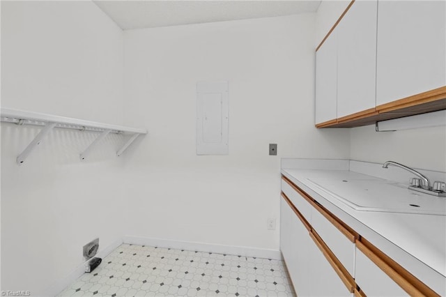 laundry room with baseboards, light floors, electric panel, cabinet space, and a sink