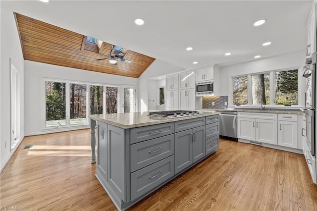 kitchen with lofted ceiling with skylight, gray cabinets, light wood-style floors, white cabinets, and stainless steel appliances