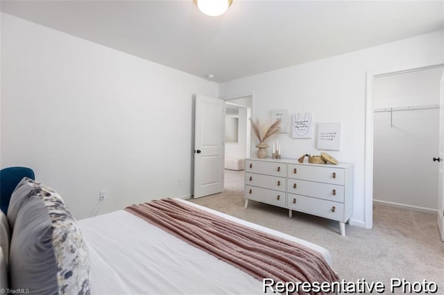 bedroom featuring light carpet, a closet, a walk in closet, and baseboards