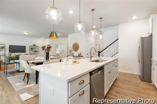 kitchen with a kitchen island with sink, white cabinets, light countertops, appliances with stainless steel finishes, and decorative light fixtures