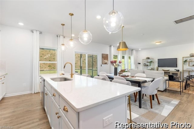 kitchen with a kitchen island with sink, pendant lighting, light countertops, and a sink