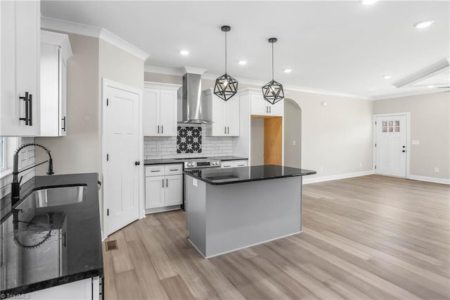 kitchen with wall chimney exhaust hood, sink, pendant lighting, white cabinets, and a kitchen island