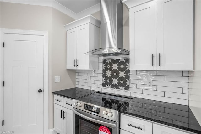 kitchen with wall chimney range hood, tasteful backsplash, dark stone counters, stainless steel range with electric stovetop, and white cabinets