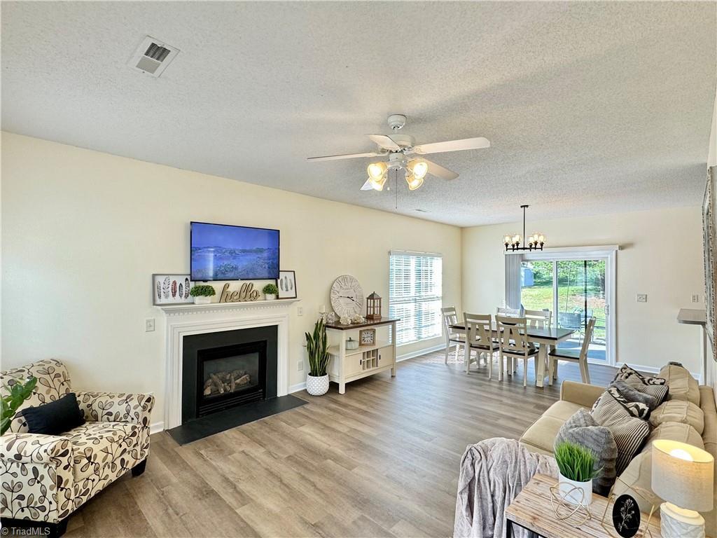 living room with ceiling fan with notable chandelier, a textured ceiling, and light hardwood / wood-style flooring