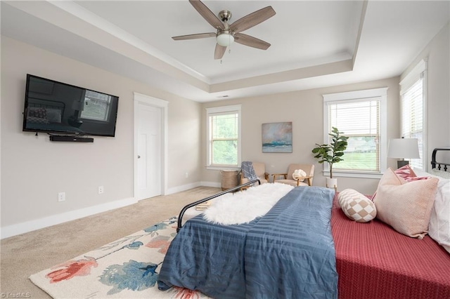 carpeted bedroom with crown molding, baseboards, ceiling fan, and a tray ceiling