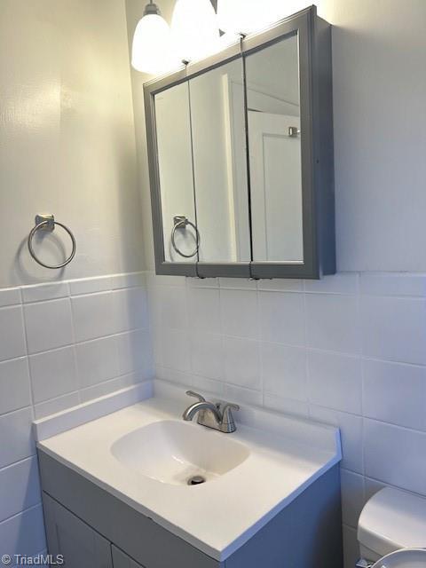 bathroom featuring toilet, tile walls, and vanity