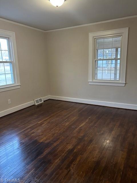 spare room featuring dark wood finished floors, visible vents, baseboards, and ornamental molding