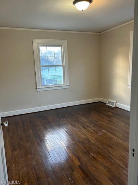 spare room featuring visible vents, baseboards, dark wood-type flooring, and crown molding