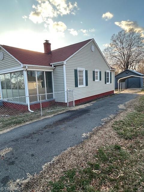 view of side of home with fence, aphalt driveway, a chimney, a sunroom, and an outbuilding