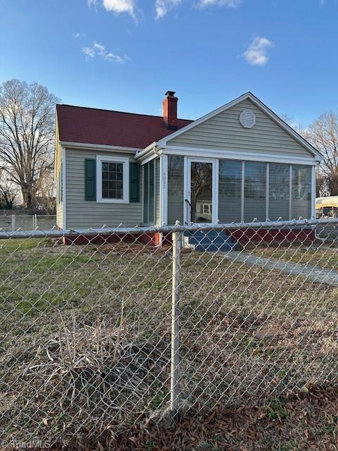 bungalow-style home with a sunroom, a chimney, and fence