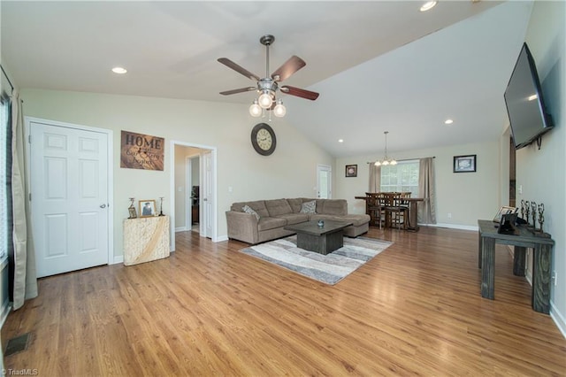 living room with ceiling fan with notable chandelier, light wood-type flooring, and vaulted ceiling