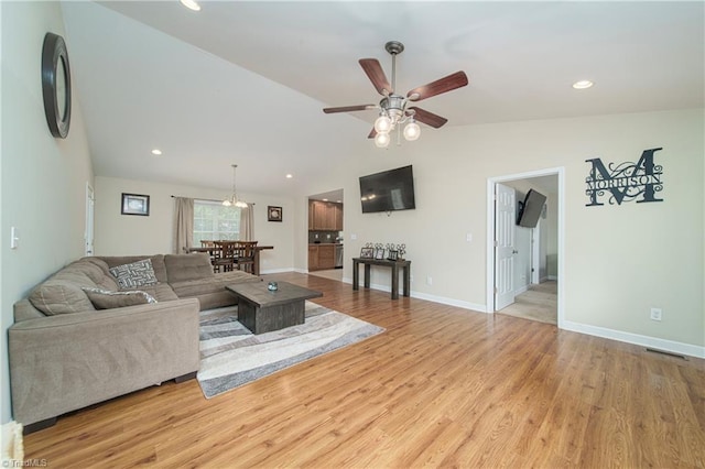 living room with ceiling fan with notable chandelier, vaulted ceiling, and light hardwood / wood-style floors