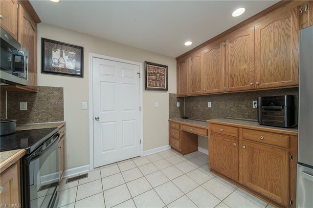 kitchen with built in desk, decorative backsplash, light tile patterned floors, and stainless steel appliances