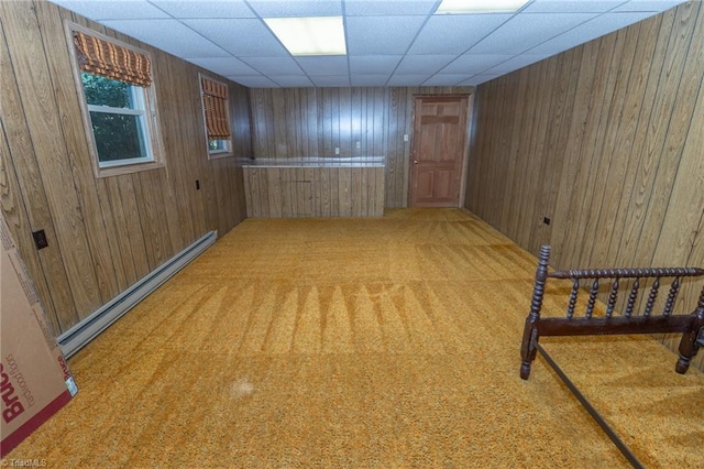 basement with a paneled ceiling, light colored carpet, baseboard heating, and wooden walls