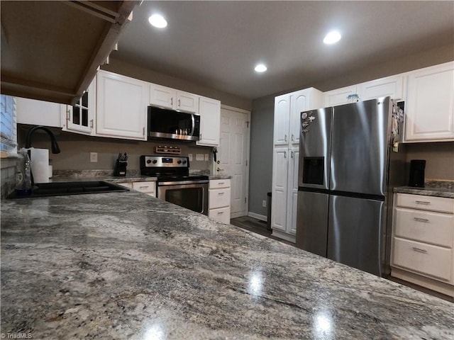 kitchen with sink, white cabinetry, stainless steel appliances, and dark stone counters