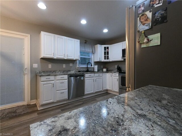 kitchen with dark wood-type flooring, white cabinets, sink, dark stone countertops, and stainless steel appliances