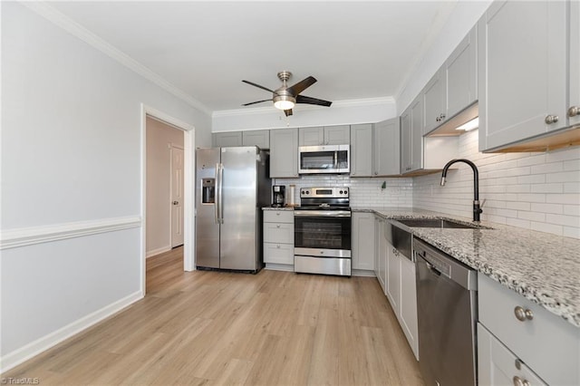 kitchen featuring appliances with stainless steel finishes, ornamental molding, light stone countertops, gray cabinets, and a sink