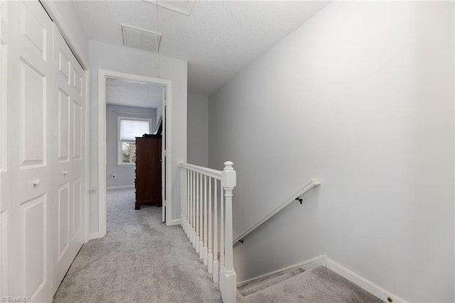 hallway with attic access, visible vents, carpet floors, and an upstairs landing