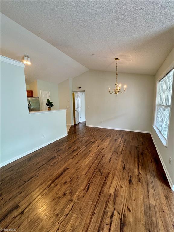 733 Rivertree Ln, Winston-Salem, NC 27103 - empty room featuring wood finished floors, a chandelier, lofted ceiling, baseboards, and a textured ceiling