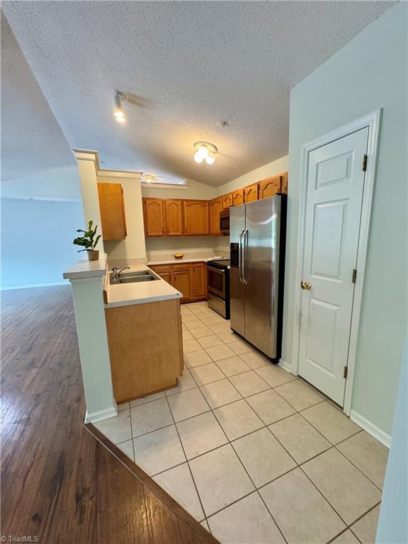 733 Rivertree Ln, Winston-Salem, NC 27103 - kitchen featuring stainless steel appliances, a peninsula, a textured ceiling, a sink, and lofted ceiling