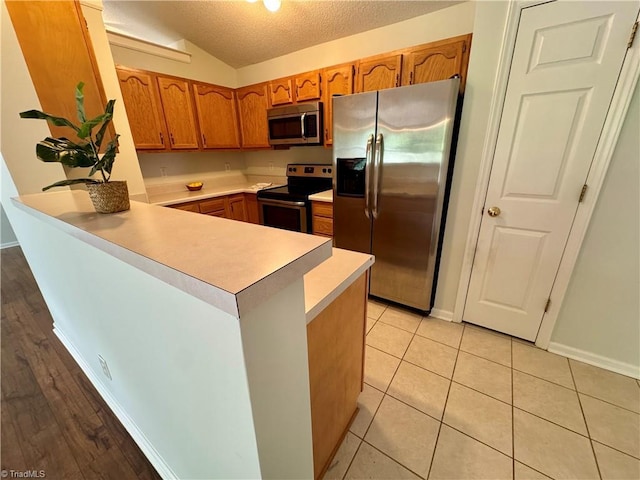 733 Rivertree Ln, Winston-Salem, NC 27103 - kitchen with appliances with stainless steel finishes, a peninsula, light countertops, brown cabinetry, and a textured ceiling