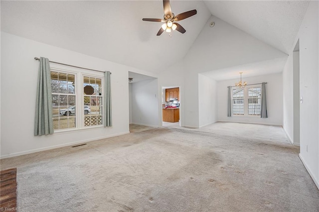 unfurnished living room with ceiling fan with notable chandelier, plenty of natural light, high vaulted ceiling, and light carpet