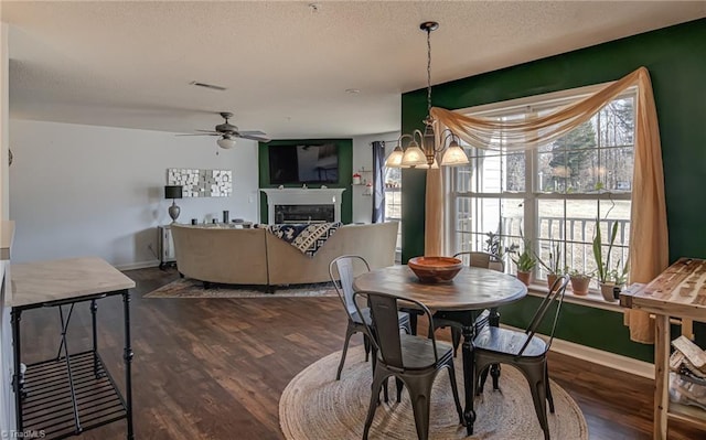 dining space with dark wood-type flooring, ceiling fan with notable chandelier, and a textured ceiling