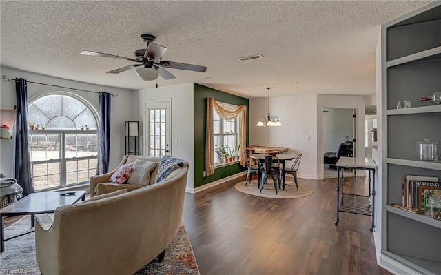 living room with built in features, ceiling fan with notable chandelier, a textured ceiling, and dark hardwood / wood-style flooring