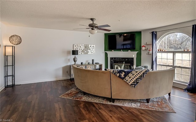 living room with dark hardwood / wood-style flooring, ceiling fan, a premium fireplace, and a textured ceiling