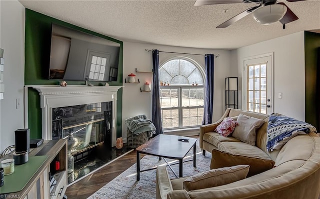 living room featuring dark hardwood / wood-style flooring, ceiling fan, a premium fireplace, and a textured ceiling