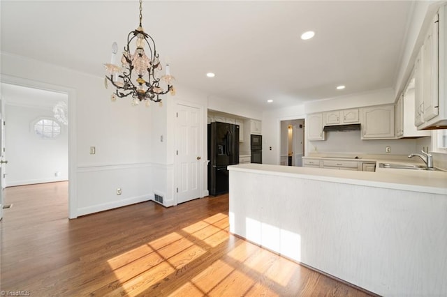 kitchen featuring sink, hanging light fixtures, white cabinets, black refrigerator with ice dispenser, and kitchen peninsula