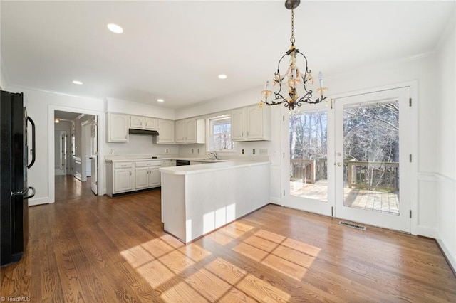 kitchen with dark wood-type flooring, sink, hanging light fixtures, kitchen peninsula, and white cabinets